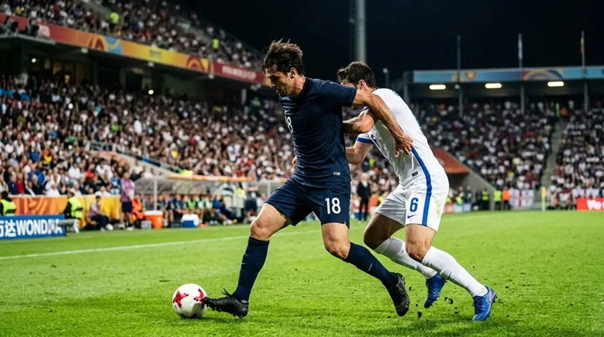 A soccer player in a plain dark kit shielding the ball from a defender during an intense World Cup match under floodlights
