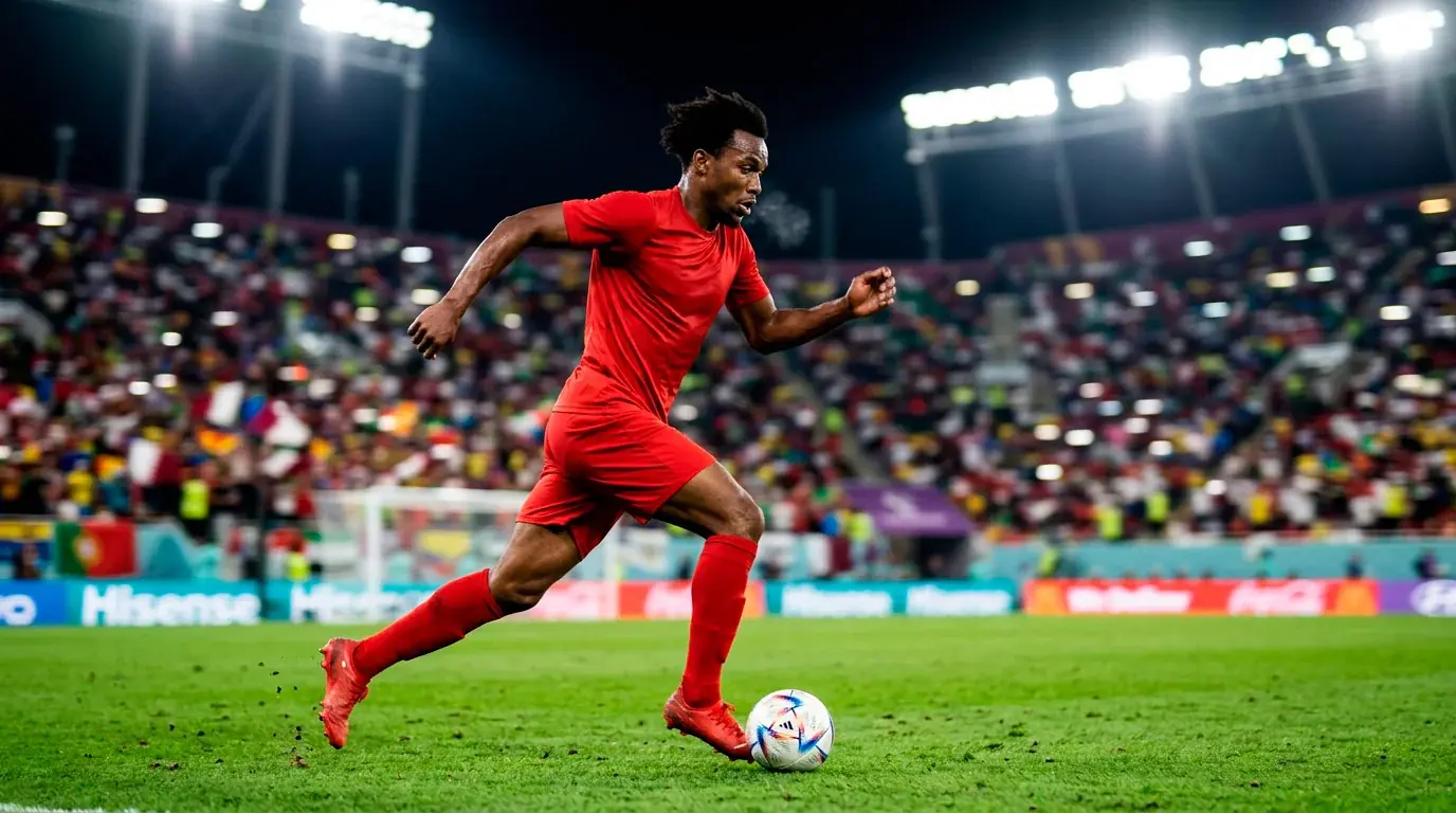 A Canadian soccer player in a red jersey sprinting with the ball during a World Cup match, crowd blurred in the background