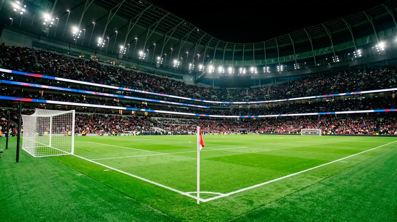 A wide view of an illuminated World Cup stadium pitch at night with empty goal and corner flag, suggesting the calm before a big international fixture